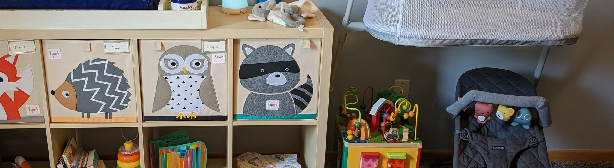 Nursery with borrowed baby gear: changing table, storage bins, bassinet, and toys